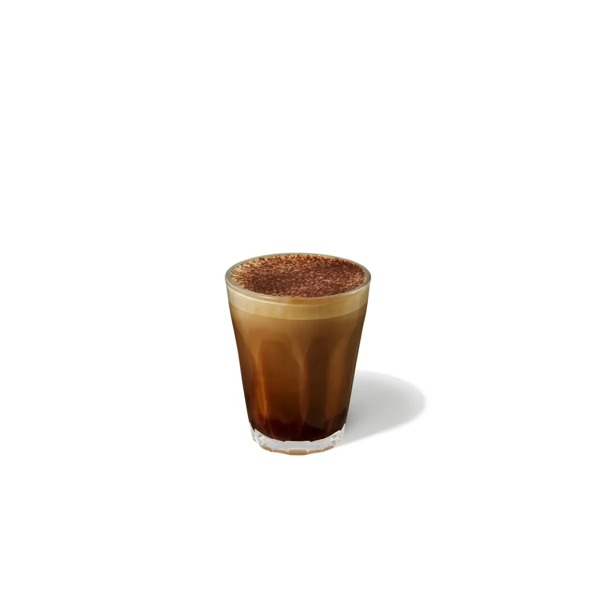 Nízky, masívny pohár s tmavohnedým espressovým základom, do ktorého sa jemne vlieva krémová pena. Vrch je posypaný kakaovým práškom – jemná hnedá vrstva, ktorá pôsobí ako dokončenie dezertnej kompozície. Nápoj je kompaktný a elegantný.