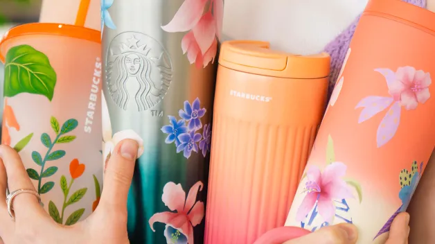 Žena s úsmevom drží v náručí päť rôznofarebných Starbucks nádob – termosiek, hrnčekov a pohárov. Sú zdobené kvetinové a rastlinnými vzormi v odtieňoch ružovej, oranžovej, zelenej a fialovej. Kolekcia pôsobí svieže a jarné. Všetky nádoby nesú logo Starbucks.