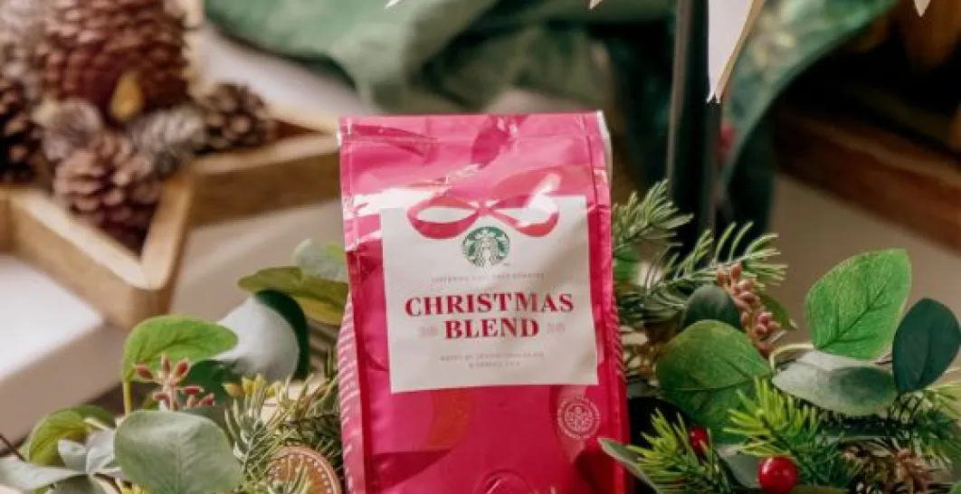 Červené vrecko zrnkovej kávy Christmas Blend, položené medzi vianočnou dekoráciou, šiškami a vetvičkami