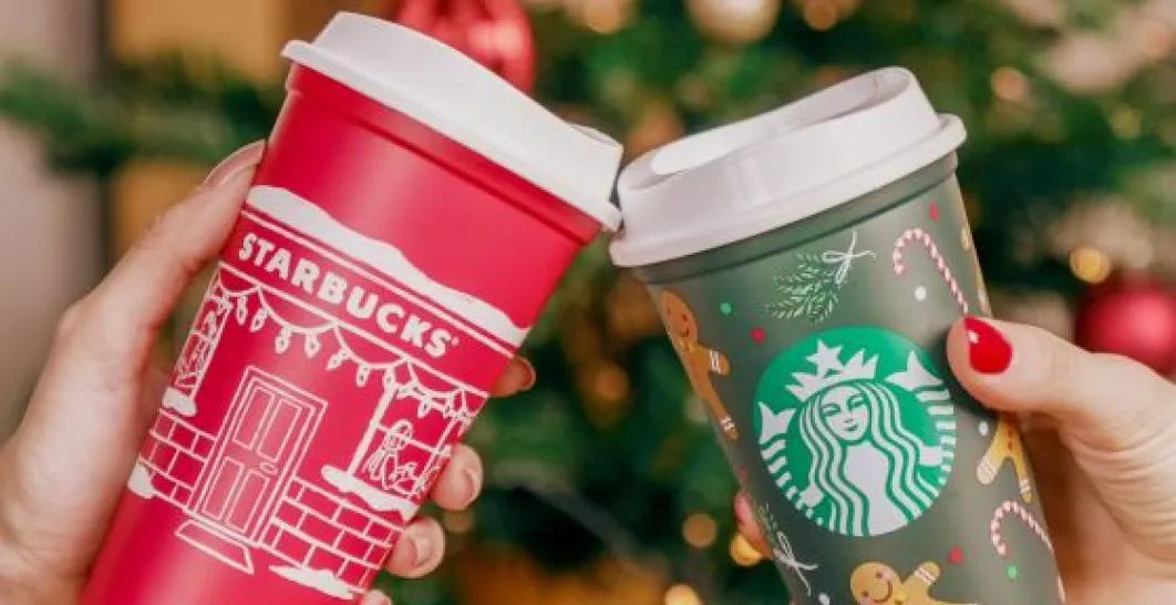 Dva opakovane použiteľné poháre Starbucks v vianočnom dizajne, vľavo červený s bielym vzorom, vpravo zelený s dizajnom medovníkových mužikov
